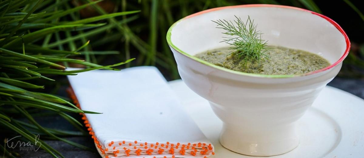 Blended green vegetable soup garnished with a sprig of fresh dill in a white ceramic bowl.