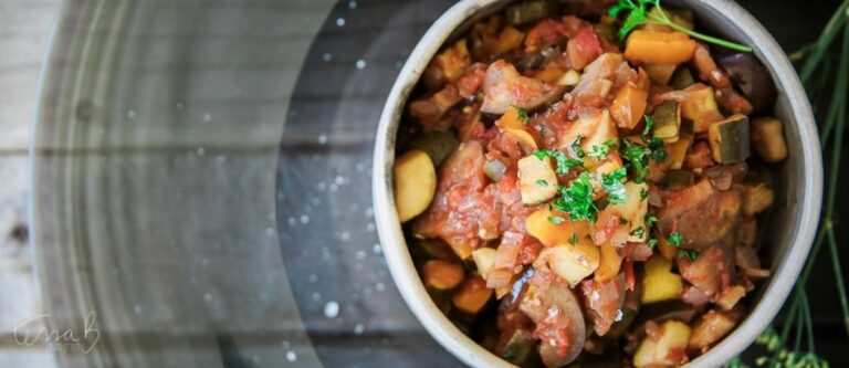 A close-up of a colorful vegetable ratatouille with diced aubergine, tomatoes, and herbs in a white ceramic bowl.
